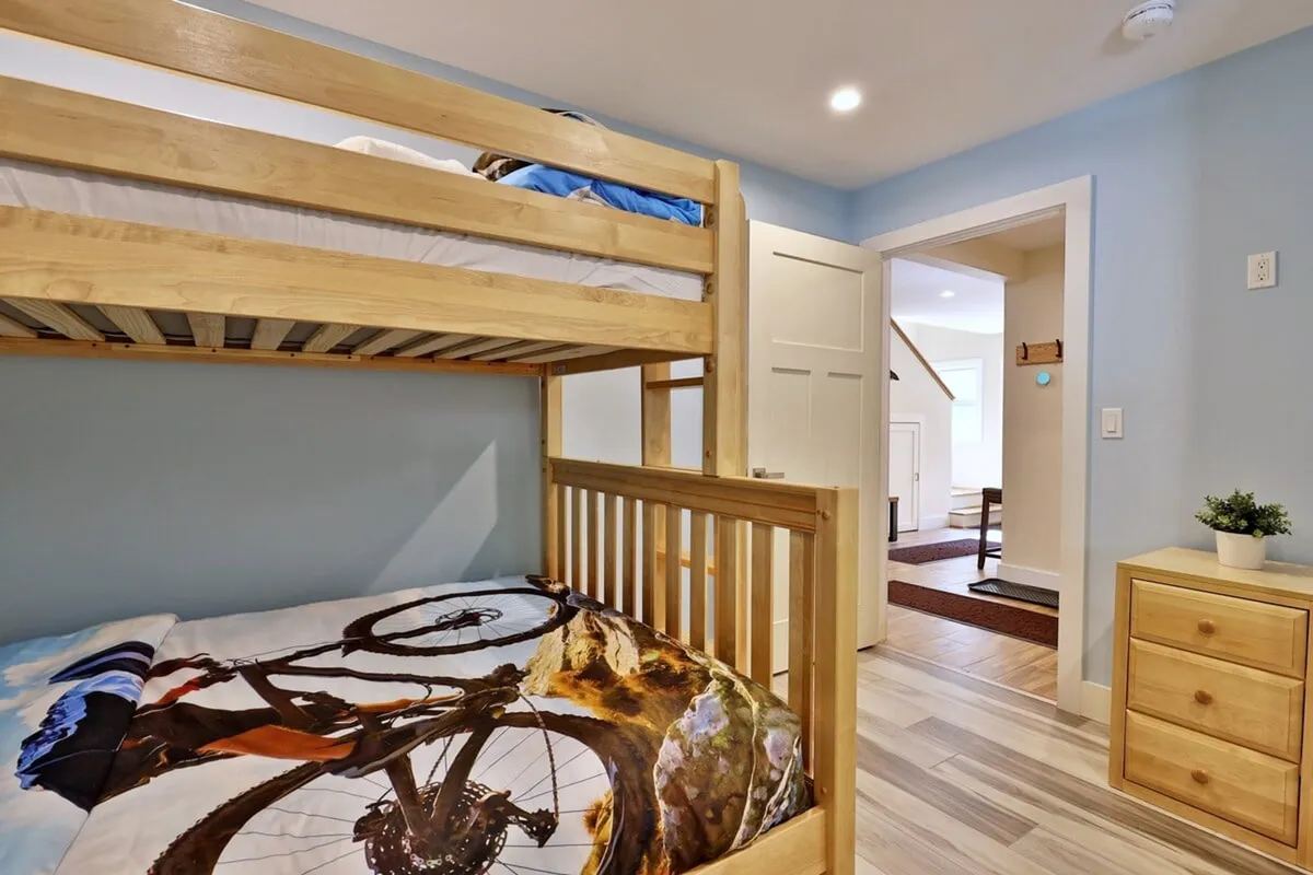 A playful and inviting room featuring a twin-over-full bunk bed with fun bicycle-themed bedding, a dresser, and an open door leading to another room. The mood is lively yet cozy, making it an ideal space for kids or friends sharing.
