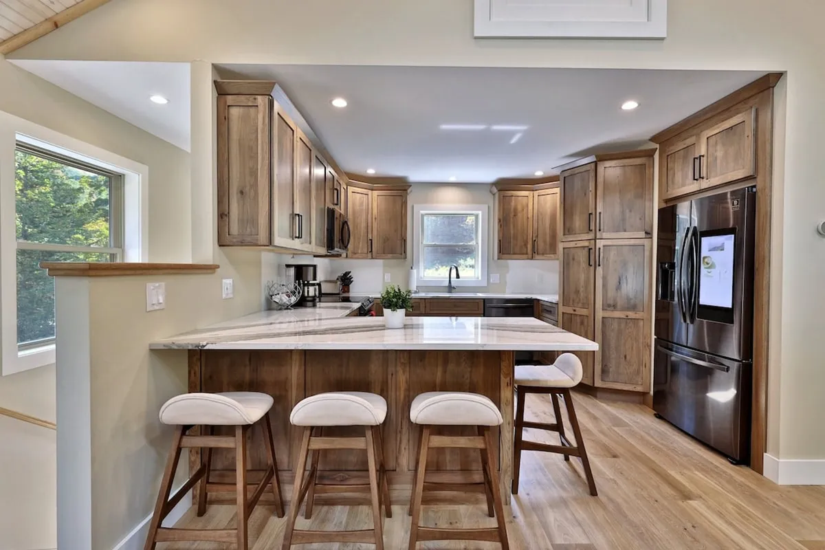 A bright, inviting kitchen scene with a central island and stools, sleek cabinetry, and a spacious countertop. The kitchen is ready for family gatherings, casual meals, or festive baking sessions, and is visually connected to the living spaces.