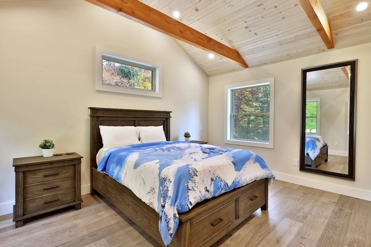 A calm and serene bedroom with a comfortable bed, mirrored wardrobe, and sunlight filtering in through a large window. The scene suggests a peaceful place for rest and relaxation, perfect for couples or solo travelers.