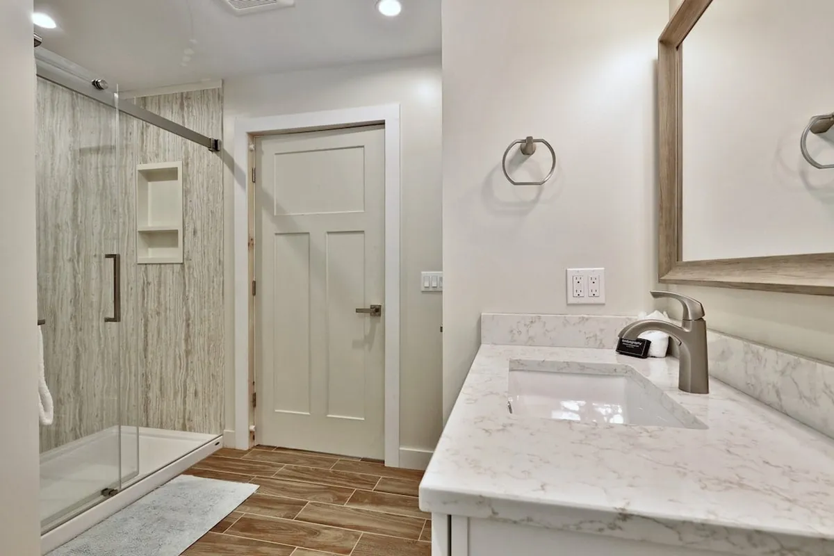 A modern bathroom with a glass shower, marble countertop, and wooden floor tiles. The setting is fresh, clean, and inviting, promising a rejuvenating experience after a day outdoors.