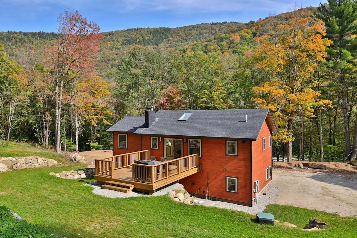 This image features a spacious wooden deck surrounded by vibrant autumn trees, with a dramatic mountain backdrop. The scene radiates tranquility and highlights the deck as an inviting space for relaxation or gatherings amidst nature’s beauty.