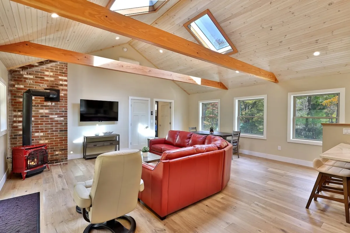 A bright, comfortable living space with a red leather sofa, brick fireplace, skylights, and large windows offering sunset or nature views. The room exudes warmth and is ideal for socializing or unwinding after winter activities.